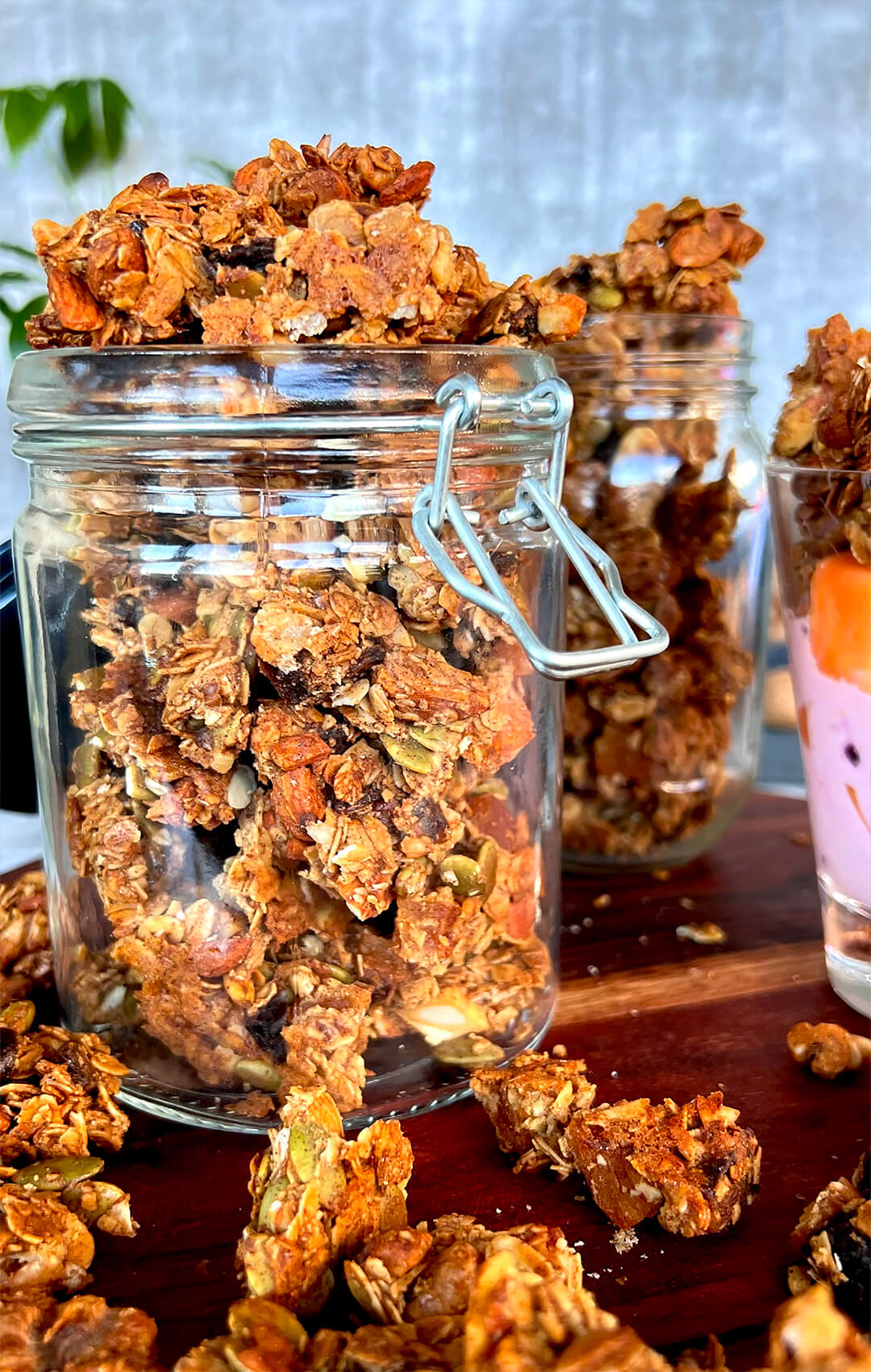 Easy Crunchy Granola Clusters on a big jar, next to a glass loaded with yogurt fresh blueberries and toped with Crunchy Granola Clusters, perfect for breakfast and snacks- gluten free, Refined Sugar Free, high protein