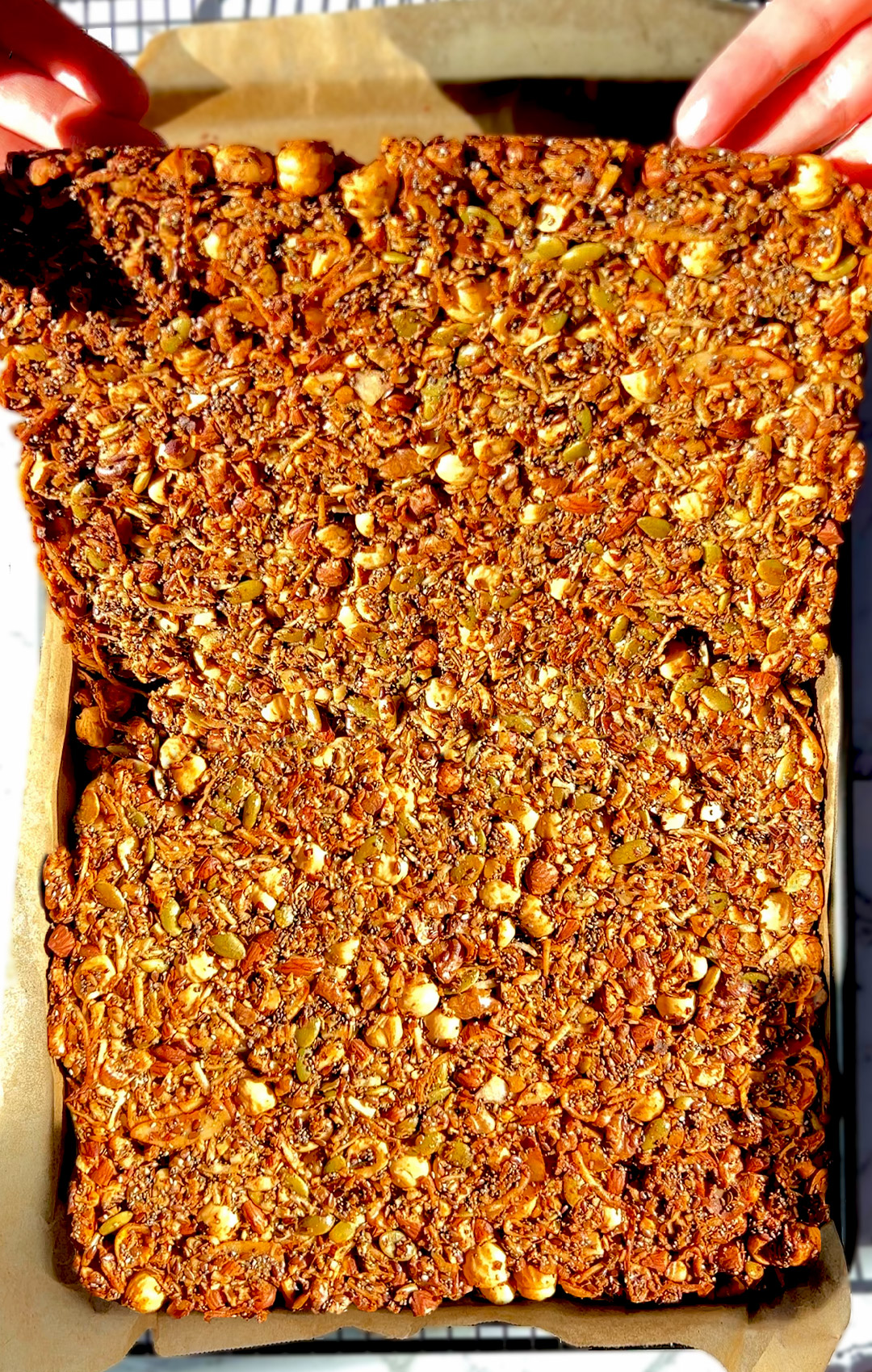 Breaking a big golden sheet of Nutty Coconut Crunch Granola by hand. Made with hazelnuts, almonds, walnuts, egg white, chia seeds, pumpkin seeds, shredded coconut, and flaxseeds. 