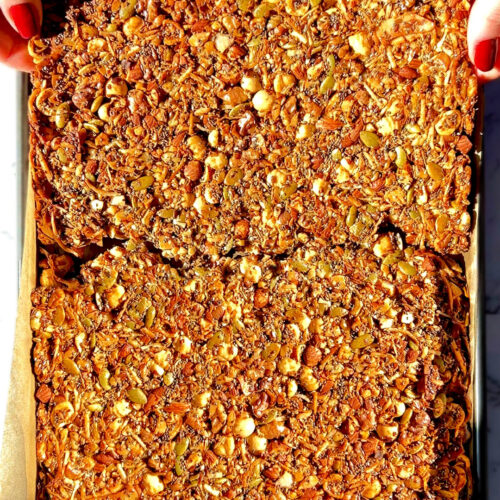 Breaking a big golden sheet of Nutty Coconut Crunch Granola by hand. Made with hazelnuts, almonds, walnuts, egg white, chia seeds, pumpkin seeds, shredded coconut, and flaxseeds