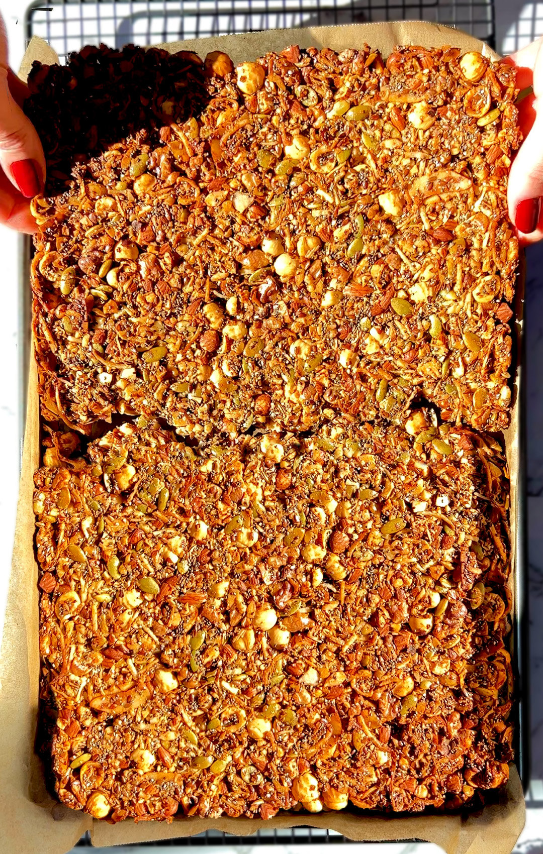 Breaking a big golden sheet of Nutty Coconut Crunch Granola by hand. Made with hazelnuts, almonds, walnuts, egg white, chia seeds, pumpkin seeds, shredded coconut, and flaxseeds