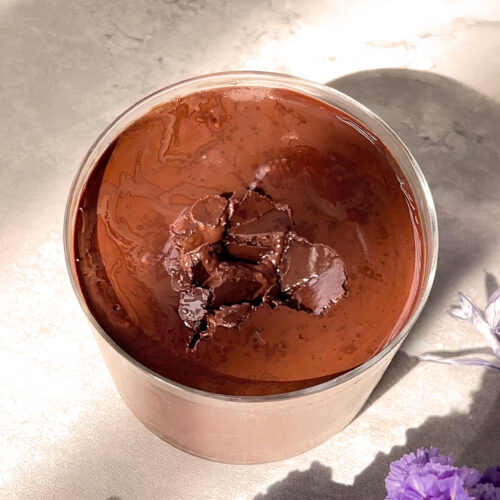 Cracked chocolate topping on chia pudding, more visibly broken after multiple spoon hits, showing soft layers underneath the soft and crunchy chocolate top