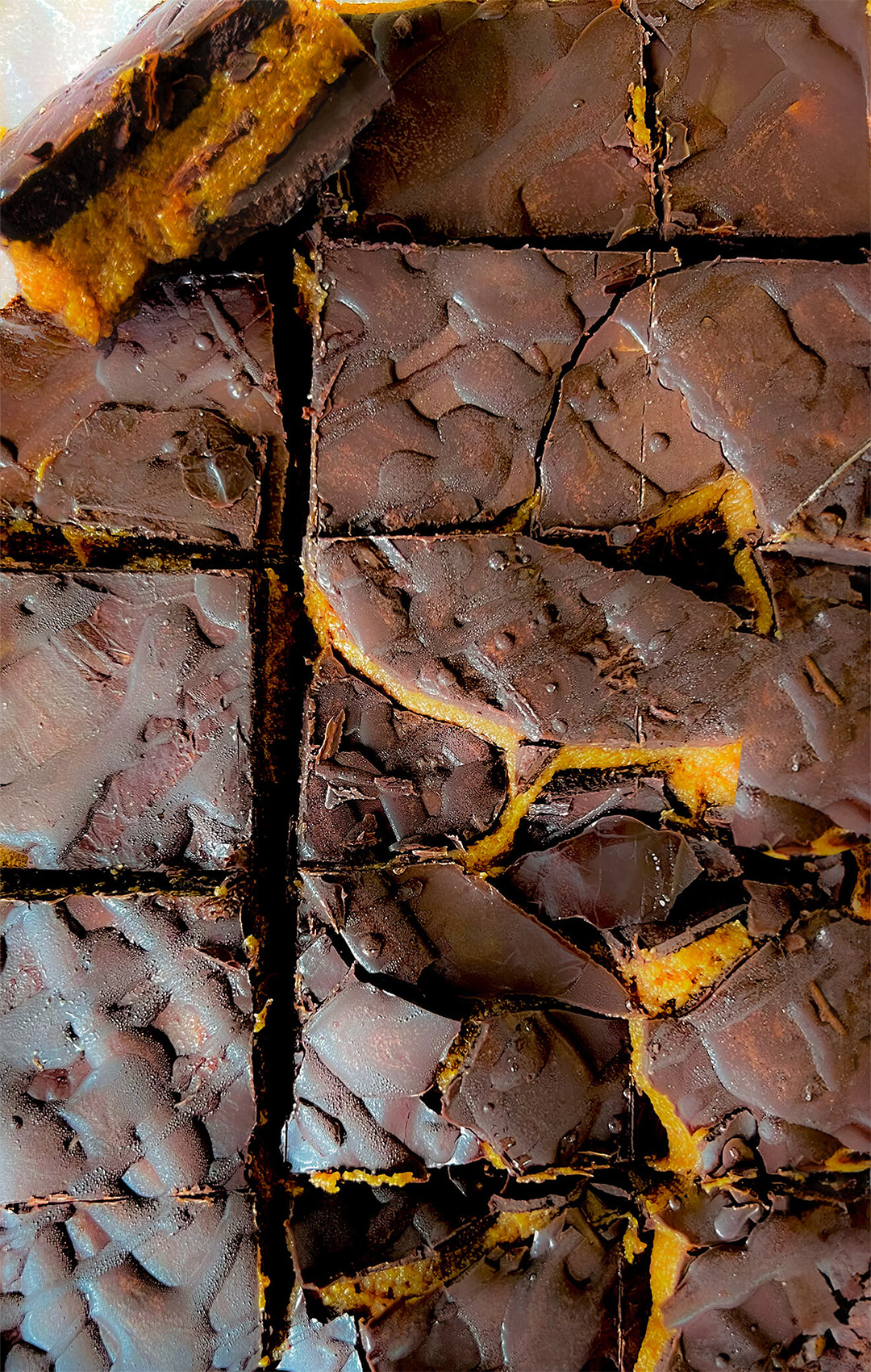 No bake chocolate date cashew caramel bars stacked in a block, showing crunchy chocolate shell and creamy caramel centre-