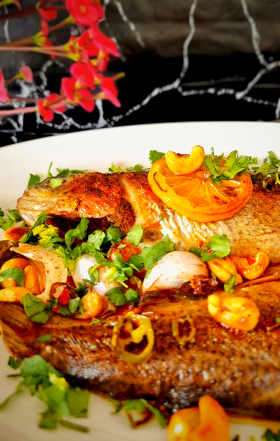 Zoomed-in view of the golden crispy-skinned whole ocean trout with roasted garlic, toasted cashews, red chilli, and roasted lemon slices topped with fresh parsley.