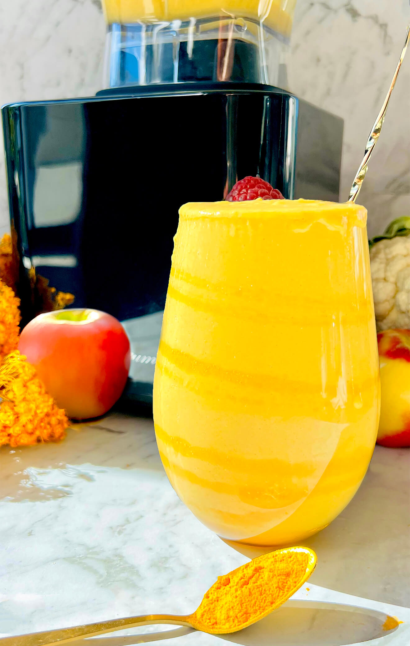 Golden smoothie with turmeric, apple, and cauliflower in the background. A beautiful gluten-free, vegan drink served in a glowing glass. Perfect as a nourishing post-workout option.