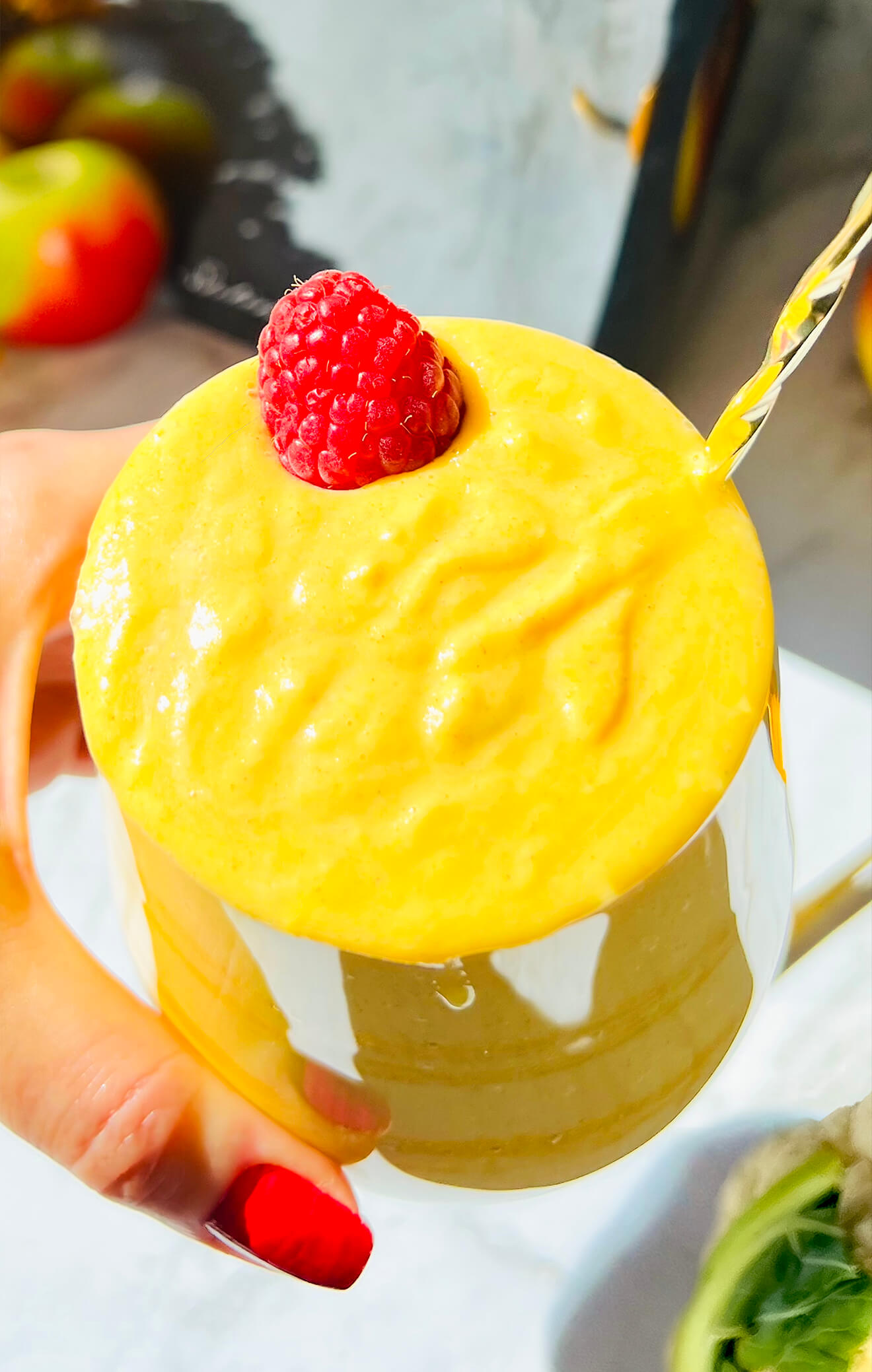 Top view of creamy golden glow smoothie in a glass with a raspberry on top, showing thick, velvety texture and antioxidant-rich blend. Made with cauliflower, Greek yogurt, turmeric powder, Apple, ginger, almond milk, and tahini, honey, pumpkin spice.