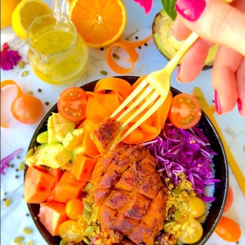 Diamond-cut marinated citrus chicken on a fork with salad bowl underneath. Juicy orange-colored chicken showing easy marinade absorption.