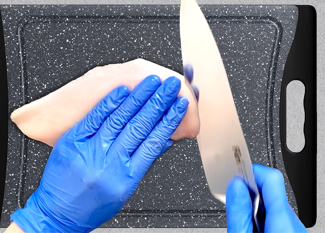 Hand holding chicken breast in place on a cutting board while the other hand positions a knife at an angle