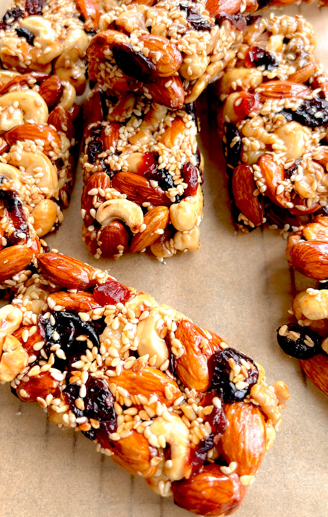 Close-up of a homemade nut and seed bar highlighting the shiny surface, toasted nuts, and sesame seed texture. Naturally sweetened, protein-rich, and ideal for clean eating or paleo diets.