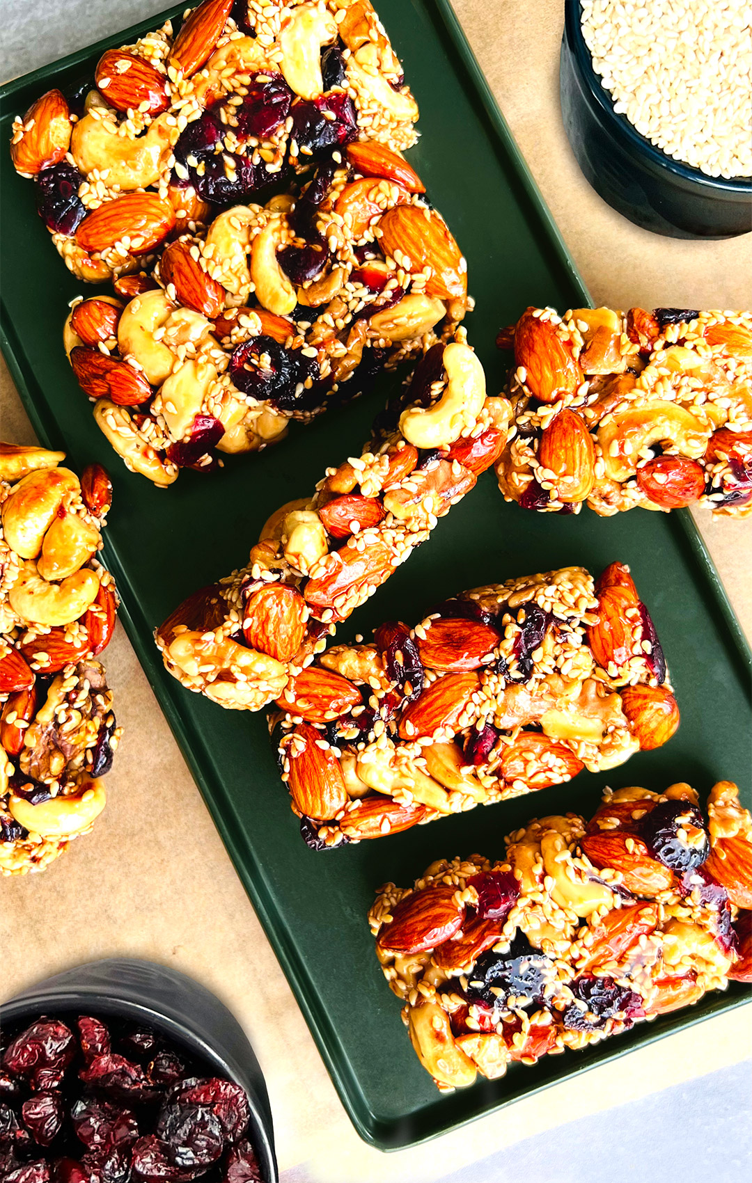 Nut and seed bars arranged on a green serving platter with cranberries and seeds in green bowls beside. Decorative healthy snack setup perfect for meal prep or casual gatherings. Vegan-friendly and no refined sugar.