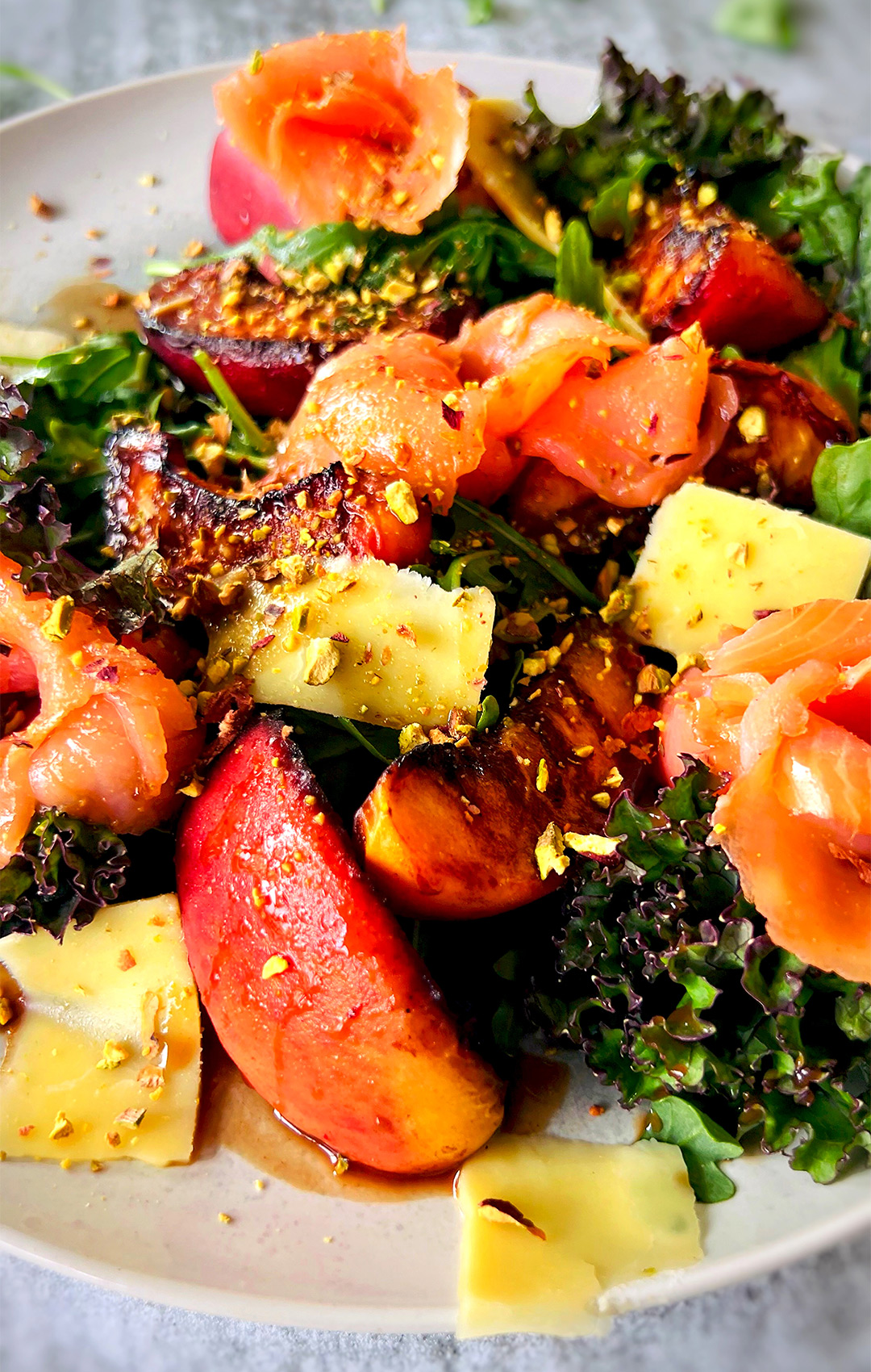 "Caramelized peach, smoked salmon, and kale topped with chopped pistachios and drizzled with honey Dijon balsamic vinaigrette on a serving plate, looking irresistibly delicious and mouthwatering.