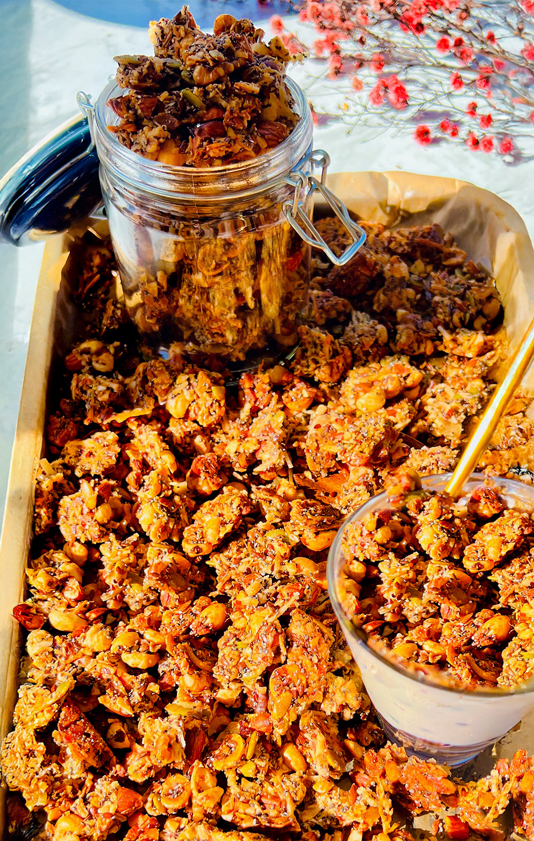 Big clusters of Nutty Coconut Crunch Granola stored in a glass jar with a serving over berry yogurt. Healthy, high-protein breakfast idea perfect for paleo and keto diets.