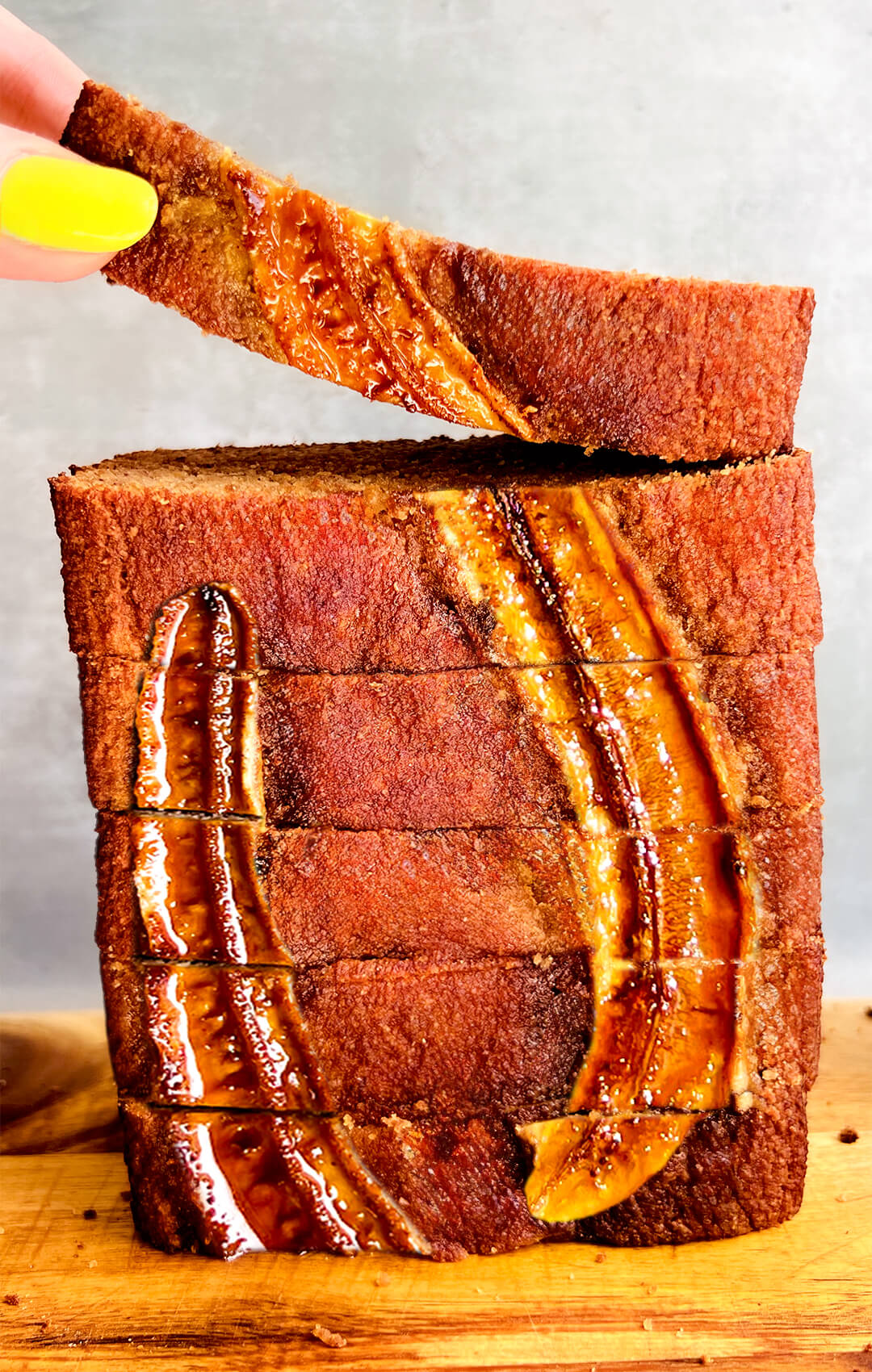 Stack of Perfect Healthy Banana Bread slices made with almond flour, coconut flour, and coconut sugar. The golden caramelized banana topping looks gorgeous and tempting, with one slice being picked to show the soft and moist texture of this healthy, Paleo gluten-free, dairy-free banana bread.