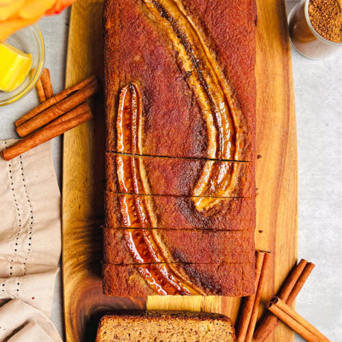 Slicing Perfect Paleo Banana Bread on a board under morning sunlight, beside a cup of coffee. The healthy gluten-free banana bread made with almond flour and coconut flour shows its fluffy, moist crumb, perfect breakfast for weekend.
