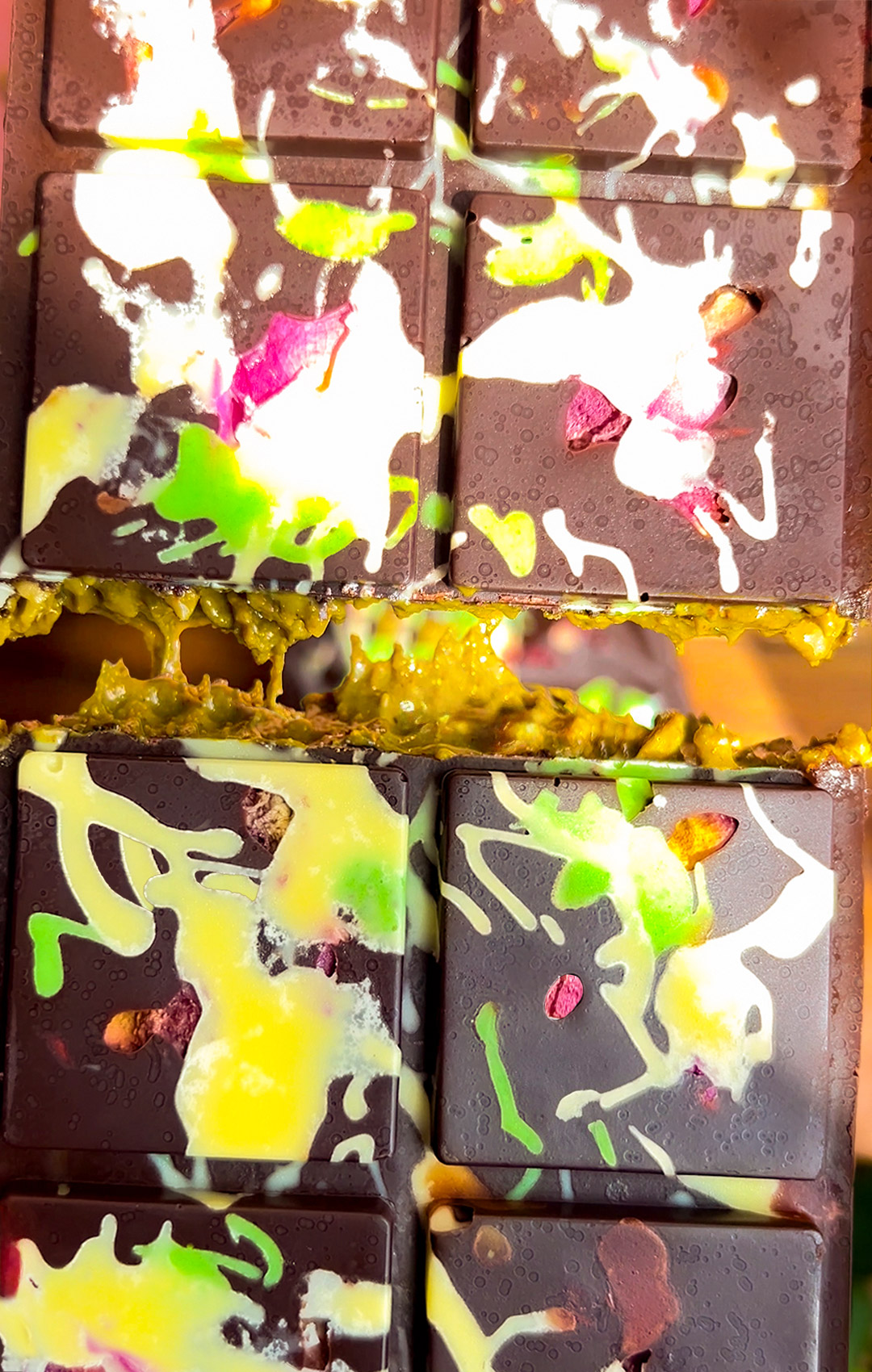 Healthy Dubai Chocolate Bars broken open and stacked, showing gooey green pistachio-tahini and toasted coconut filling. Decorated dark chocolate shell with white and green drizzle and rose petals. Creamy, crunchy, smooth, and gooey for a unique multi-textural bite. Healthy, low carb, gluten free, refined sugar free, keto and paleo friendly.