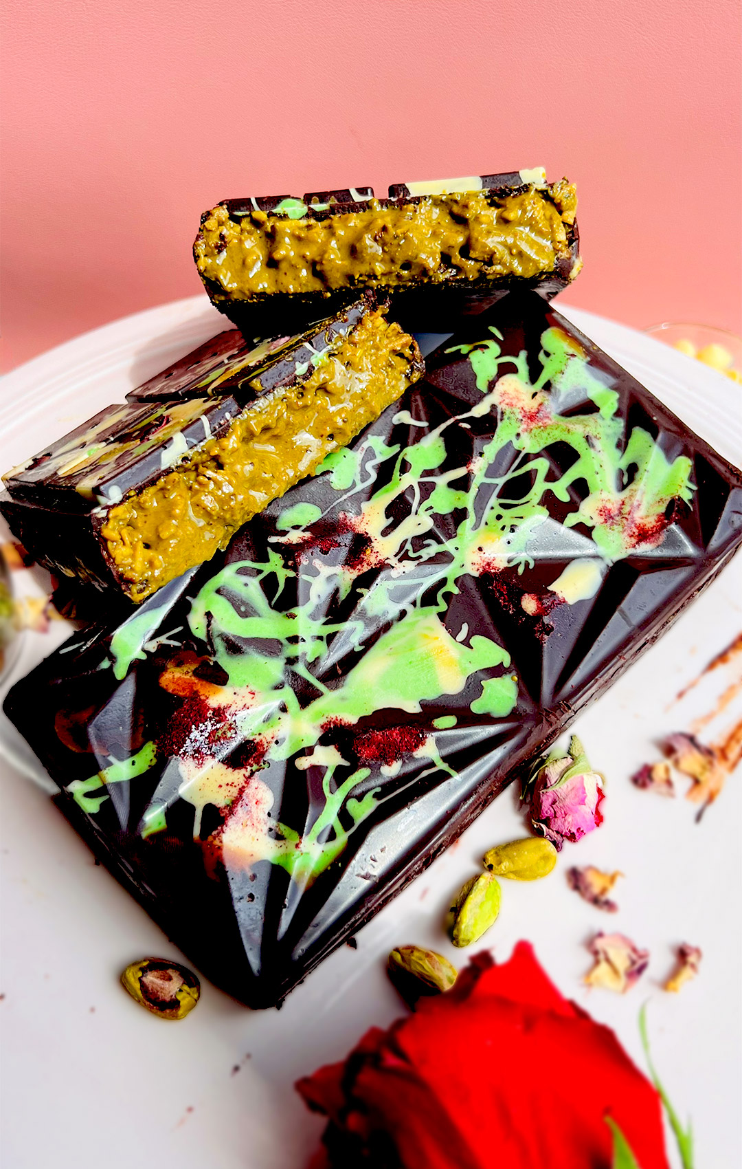 Sliced Healthy Dubai Chocolate Bars displayed on a glossy geometric block, decorated with raspberry powder and white-green drizzle. Vibrant green pistachio cream with tahini and toasted coconut adds creamy crunch inside. Gluten free, low carb, keto option, paleo, refined sugar free.