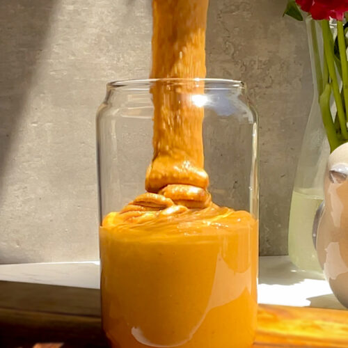 Easy Homemade Roasted Peanut Butter being poured into a glass jar, smooth and runny with golden roasted peanuts, no oils, no preservatives, no sugar, pure nutty taste. naturally nutty taste that makes every spoonful irresistible.simple one-ingredient recipe