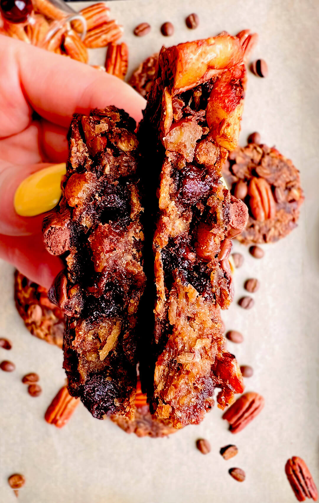 Close up of a Banana Oatmeal Cookies with Coffee & Pecans broken in half in a hand showing the gooey chewy centre. Healthy no sugar added, oatmeal cookie with pecans and chocolate chips for breakfast or a