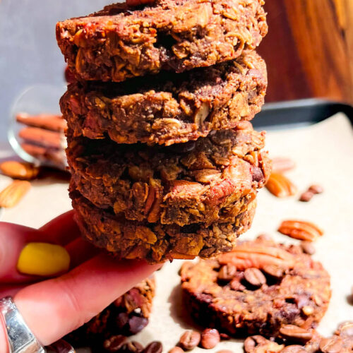 Zoom in Hand holding a tall stack of chewy Banana Oatmeal Cookies with Coffee & Pecans. Healthy no sugar added breakfast oatmeal cookies ideal for clean eating and weight loss snacks also meal prep.. They are gluten free, no oil, no dairy and naturally sweet with banana.