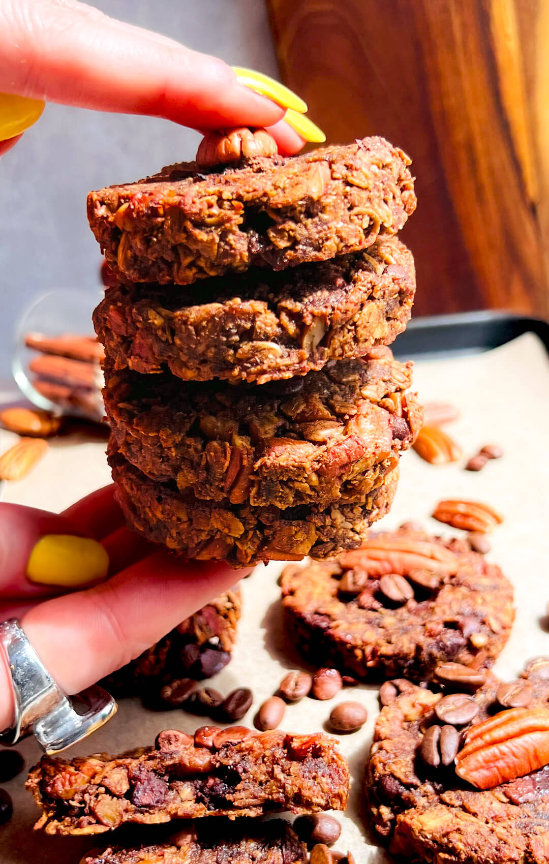 Zoom in Hand holding a tall stack of chewy Banana Oatmeal Cookies with Coffee & Pecans. Healthy no sugar added breakfast oatmeal cookies ideal for clean eating and weight loss snacks also meal prep.. They are gluten free, no oil, no dairy and naturally sweet with banana.