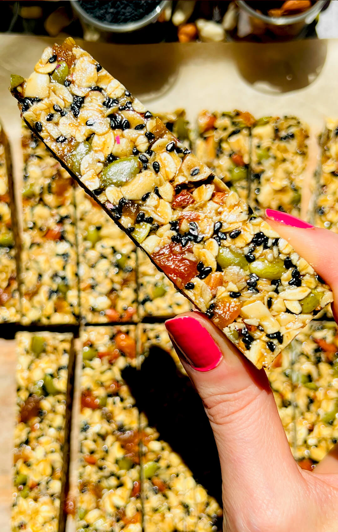 hand holding a chewy oat and honey granola bar with tahini, healthy gluten free and naturally sweetened snack bar with sweet apricot, crunchy pumpkin seeds, nutty almonds and black sesame