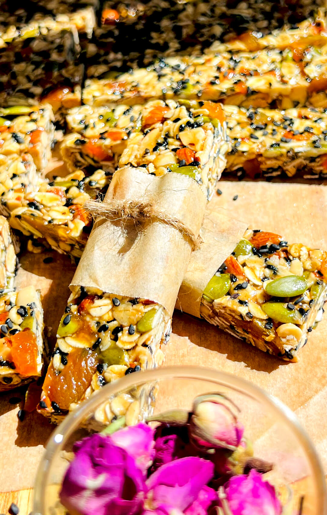 Stack of Easy homemade oat and nut granola bars with honey, tahini and rosewater, gluten free and naturally sweetened healthy snack with warm spices and chewy texture, perfect healthy, gluten free decorating with rose petal, on sunlight to show the shiny chewy texture