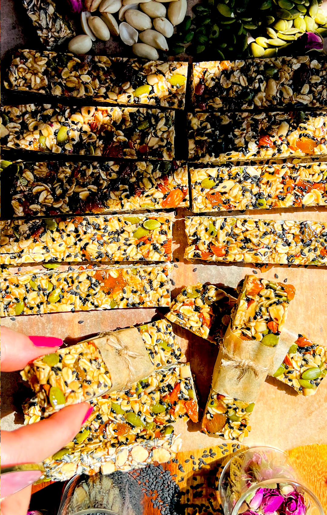 hand reaching toward oat and nut granola bars cut into bars with honey, tahini and rosewater, gluten free and naturally sweetened, showing chewy texture and visible seeds, on a wooden board, chewy gluten free and naturally sweetened, prepared for healthy meal prep