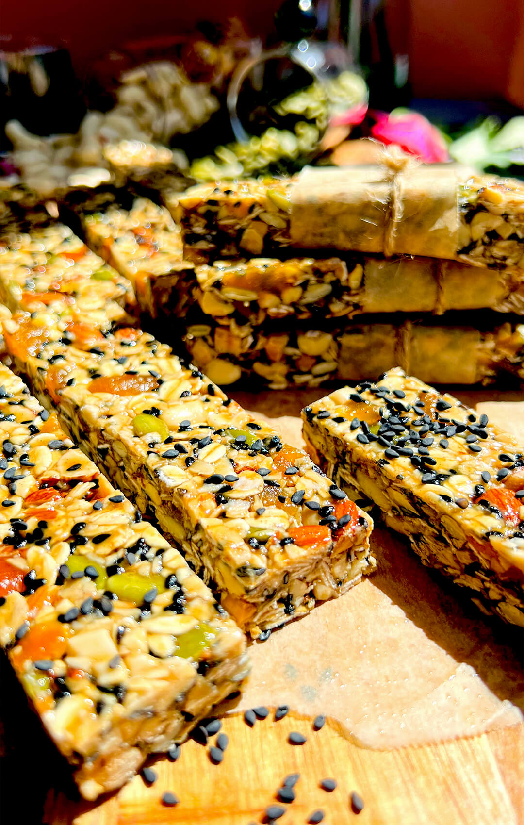 stacked chewy oat granola bars with honey and tahini and rose water, gluten free and naturally sweetened, sunlight emphasizing the glossy texture and seeded surface, some of them wrapped up on baking paper