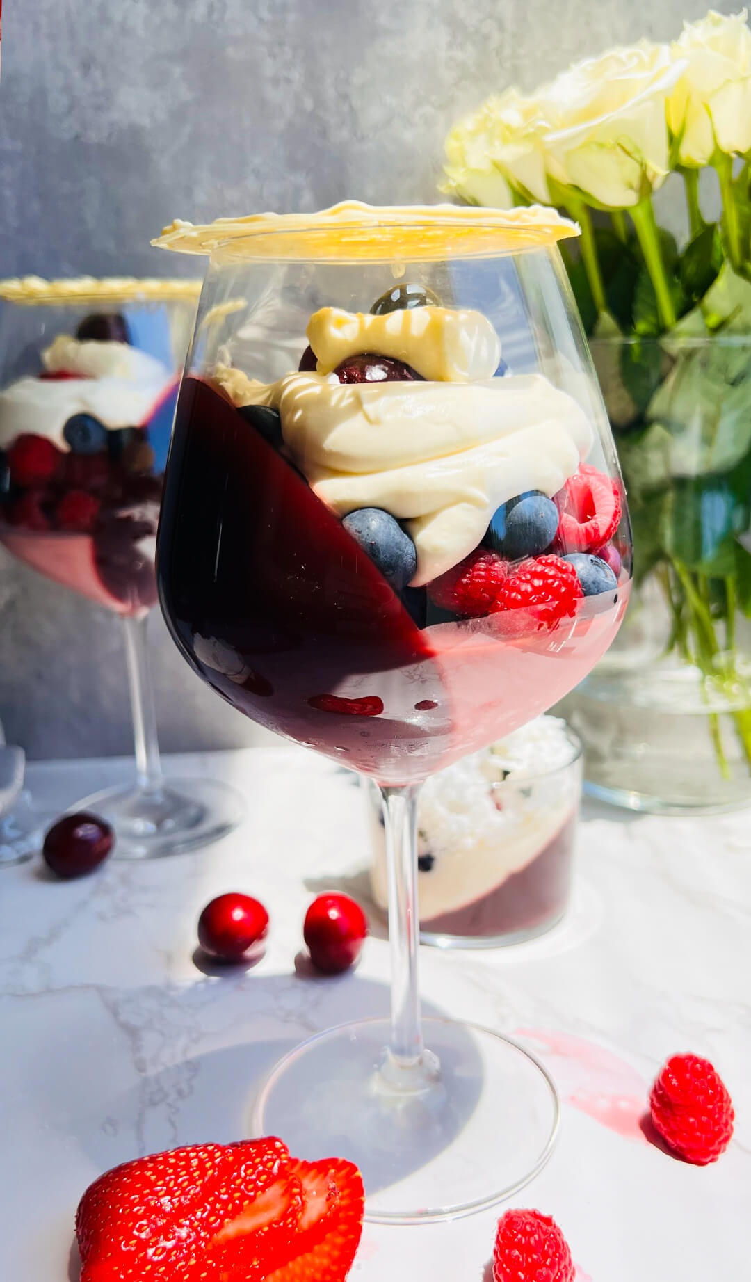 A festive sugar-free pomegranate berry trifle served in a wine glass, featuring angled pomegranate jelly, a silky flummery layer, fresh berries, whipped cream, and a delicate white chocolate lace on top. Refreshing, creamy, and light, this dessert is made with real ingredients and no refined sugar. Gluten free, low carb friendly, and perfect for holidays and special occasions.
