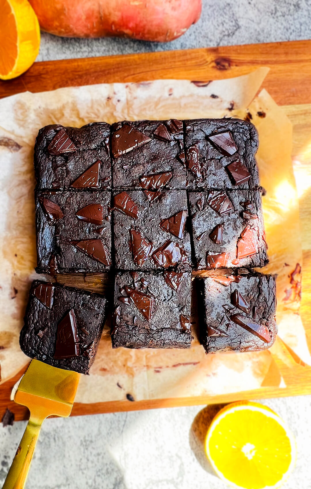 Fudgiest sweet potato chocolate brownies cut into squares on timber board with orange slice and spatula, healthy, flourless, gluten free, paleo, low-carb dessert.