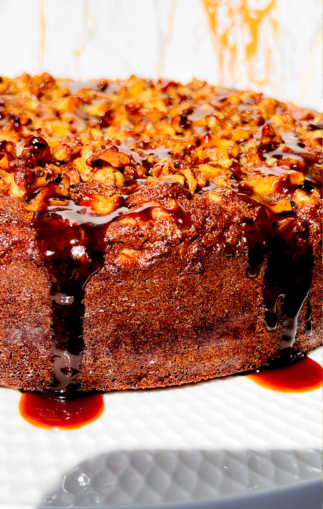 zoom in Sticky apple pudding cake made with almond flour, featuring a deep golden crispy edges, caramelised apple and walnut topping, and coconut caramel sauce dripping over the sides. Healthy, gluten-free, dairy-free, and refined sugar-free dessert.