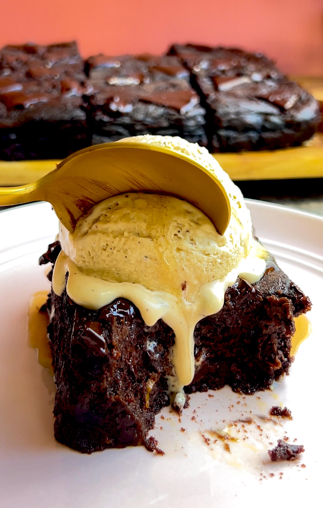 closeup to a thick, Warm sweet potato chocolate brownie on a plate with melting vanilla ice cream, ultra fudgy, spoon in, show showing gooey texture, it is a healthy brownie that is flourless and gluten free with no sugar.