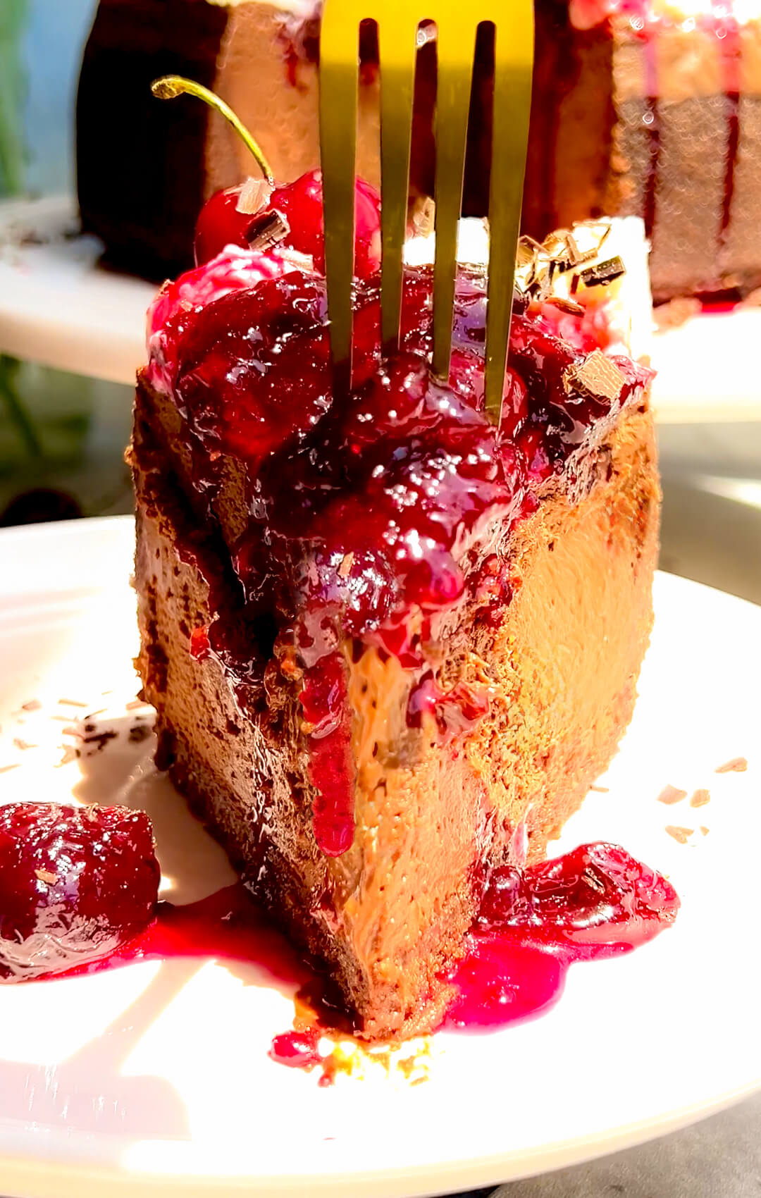 Fork cutting into a silky chocolate French forest cheesecake slice, showing a smooth, decadent chocolate cheesecake texture with glossy sugar-free homemade cherry topping