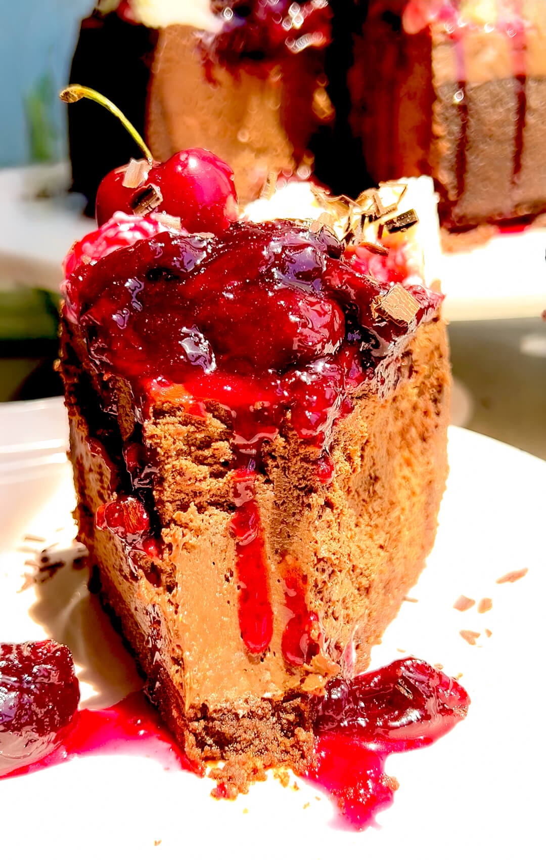 Gluten-free French forest cheesecake slice with a tall, clean structure, deeply chocolatey cheesecake filling, crunchy chocolate base, and glossy homemade cherry topping made with monkfruit, drizzling cherry sauce