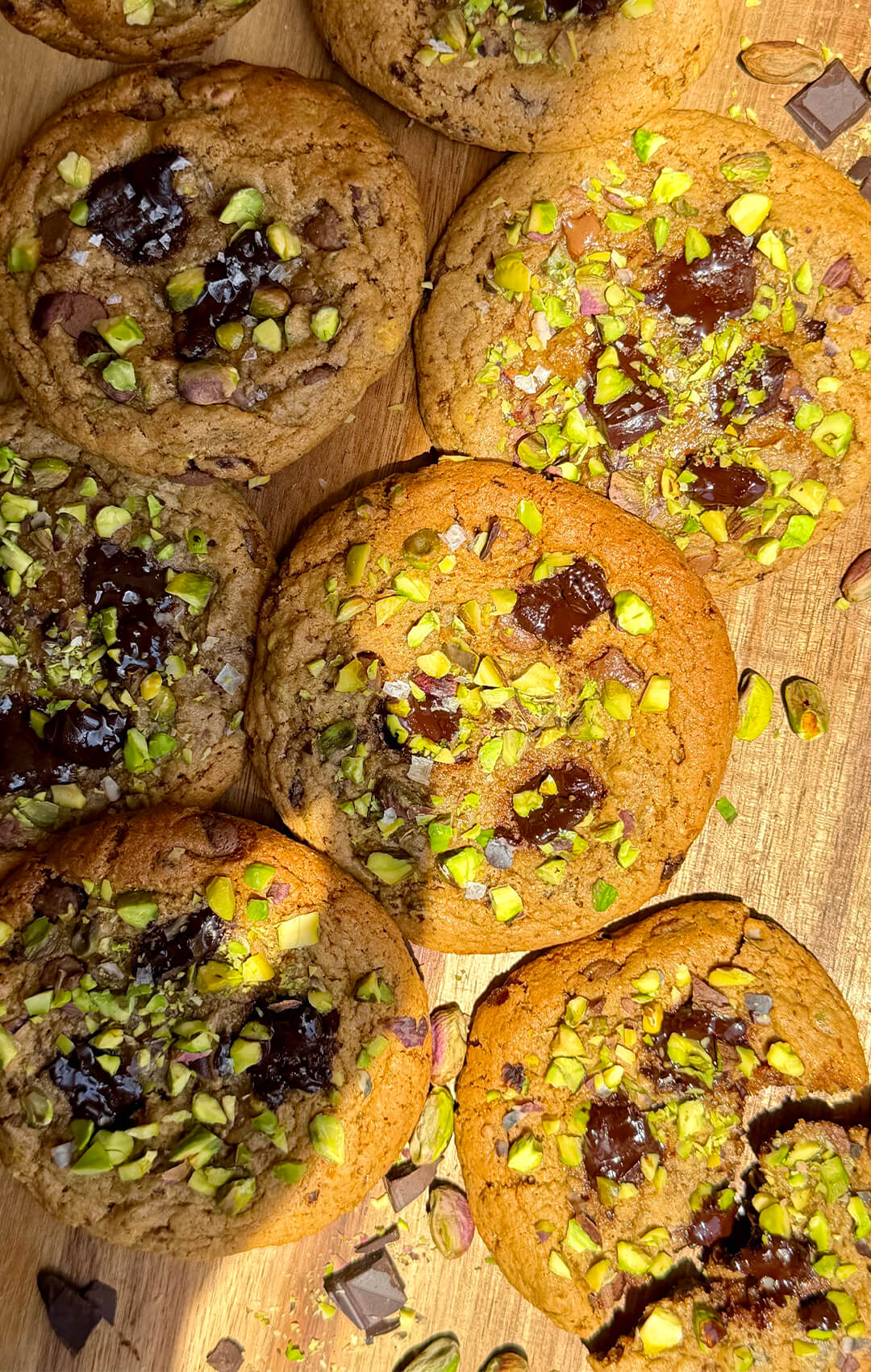 Healthy pistachio chocolate chunk cookies arranged on wooden board with chopped pistachios and dark chocolate pieces. Gluten-free grain-free dessert with bakery-style texture