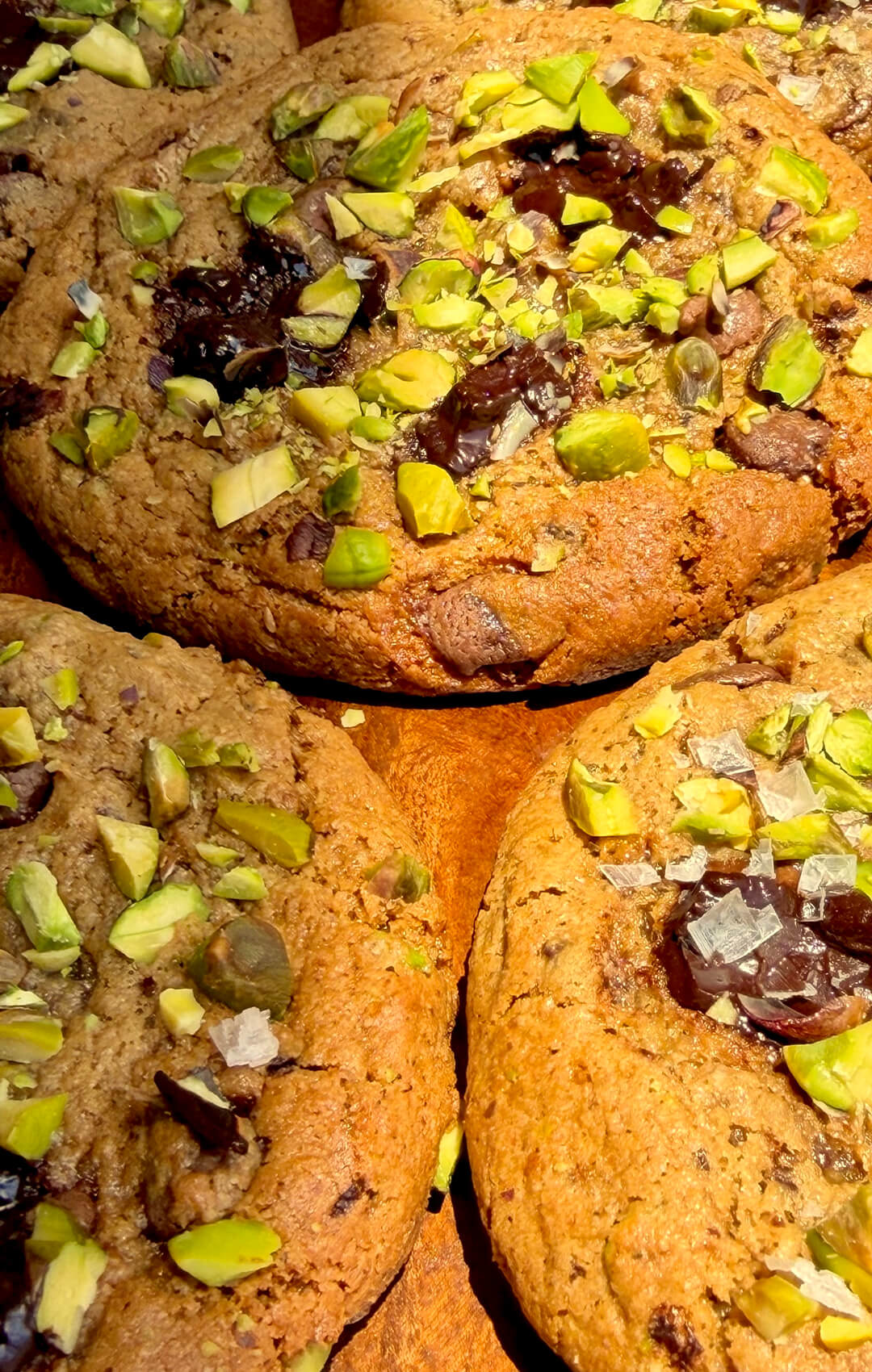 Detailed texture of pistachio chocolate chunk cookie showing caramelised crispy edges, soft centre and glossy melted dark chocolate pieces.