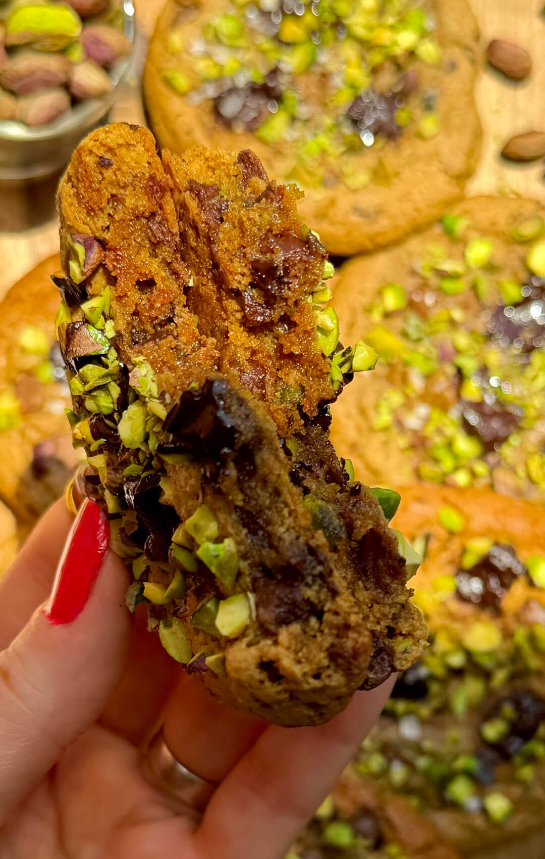 Healthy pistachio chocolate chunk cookie broken open to reveal soft centre, melty chocolate chips and crunchy pistachio topping.