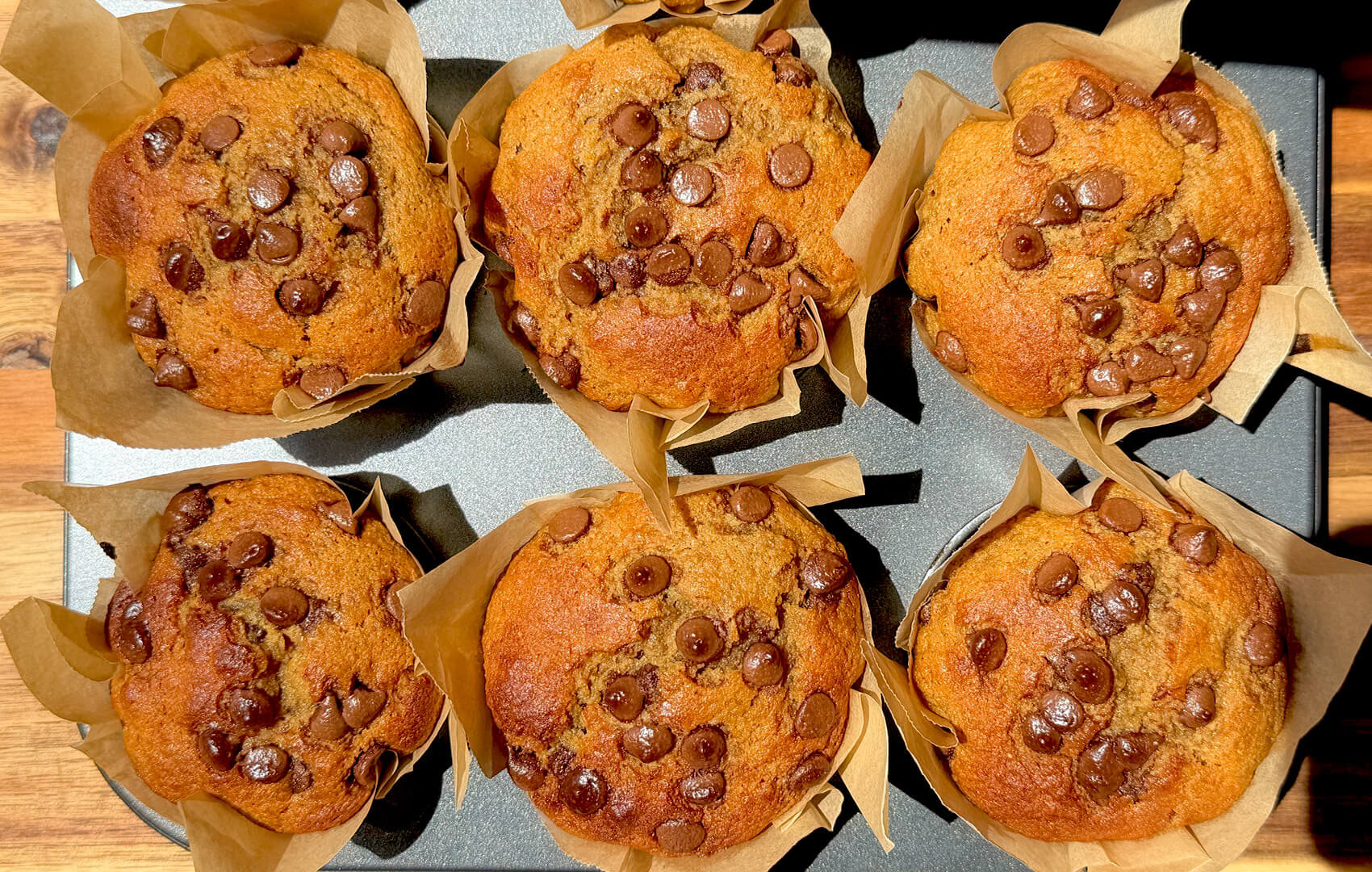 Overhead tray of Banana Oat Chocolate Chip Muffins with golden tops and chocolate chips, quick and easy high protein high fiber muffins made with oat flour and lupin flour.