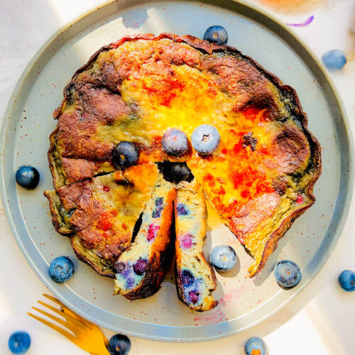 Fluffy blueberry omelet on a plate, golden and puffy with juicy blueberries and golden caramelised edges, Ready in 10 minutes with simple ingredients. flourless, keto, gluten-free, sugar-free healthy, breakfast or brunch, it looks like a café-style breakfast on a plate.