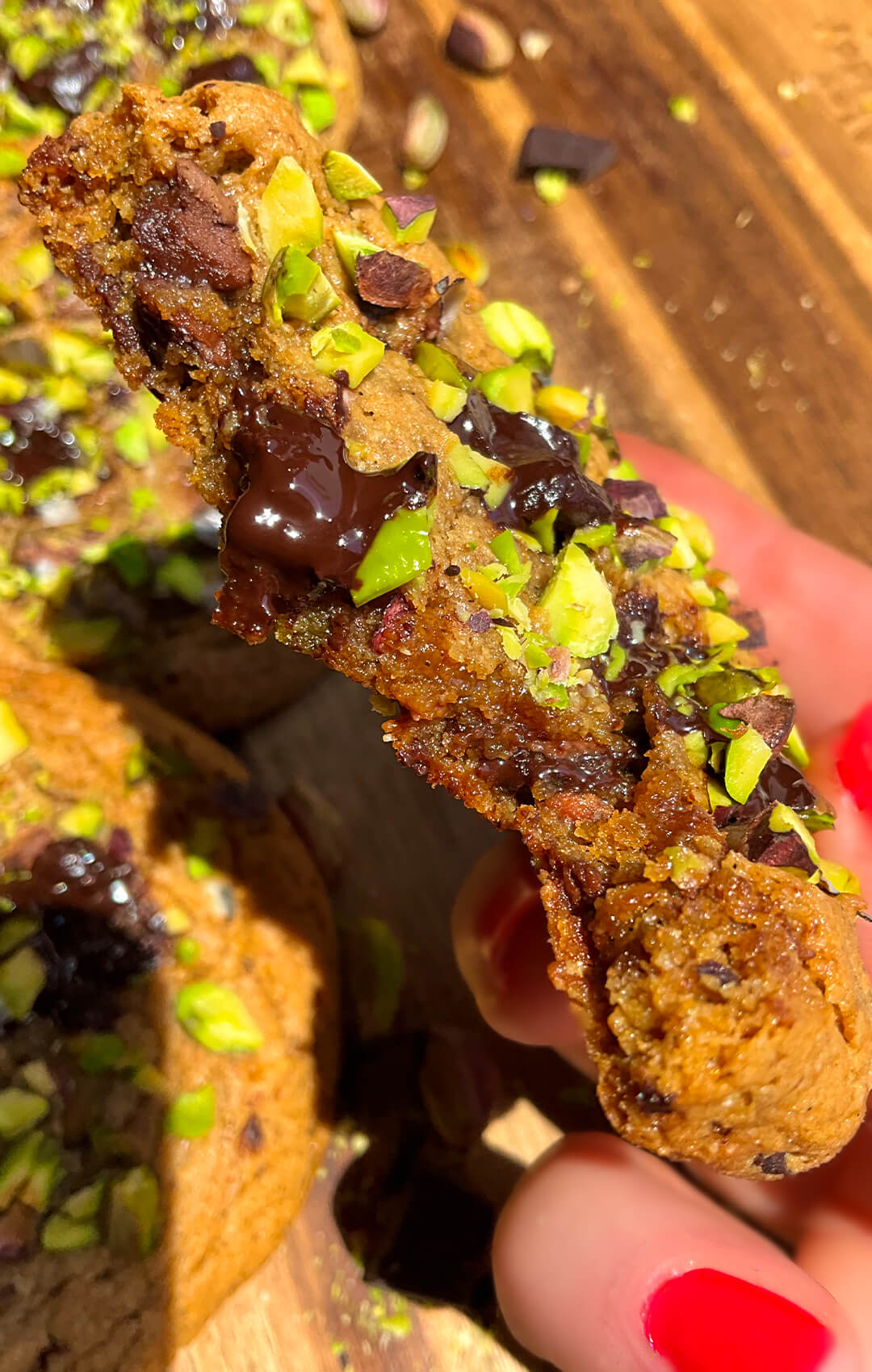 Close-up of melty dark chocolate chunks and chopped pistachios on thick bakery-style cookie with crispy caramelised edges.
