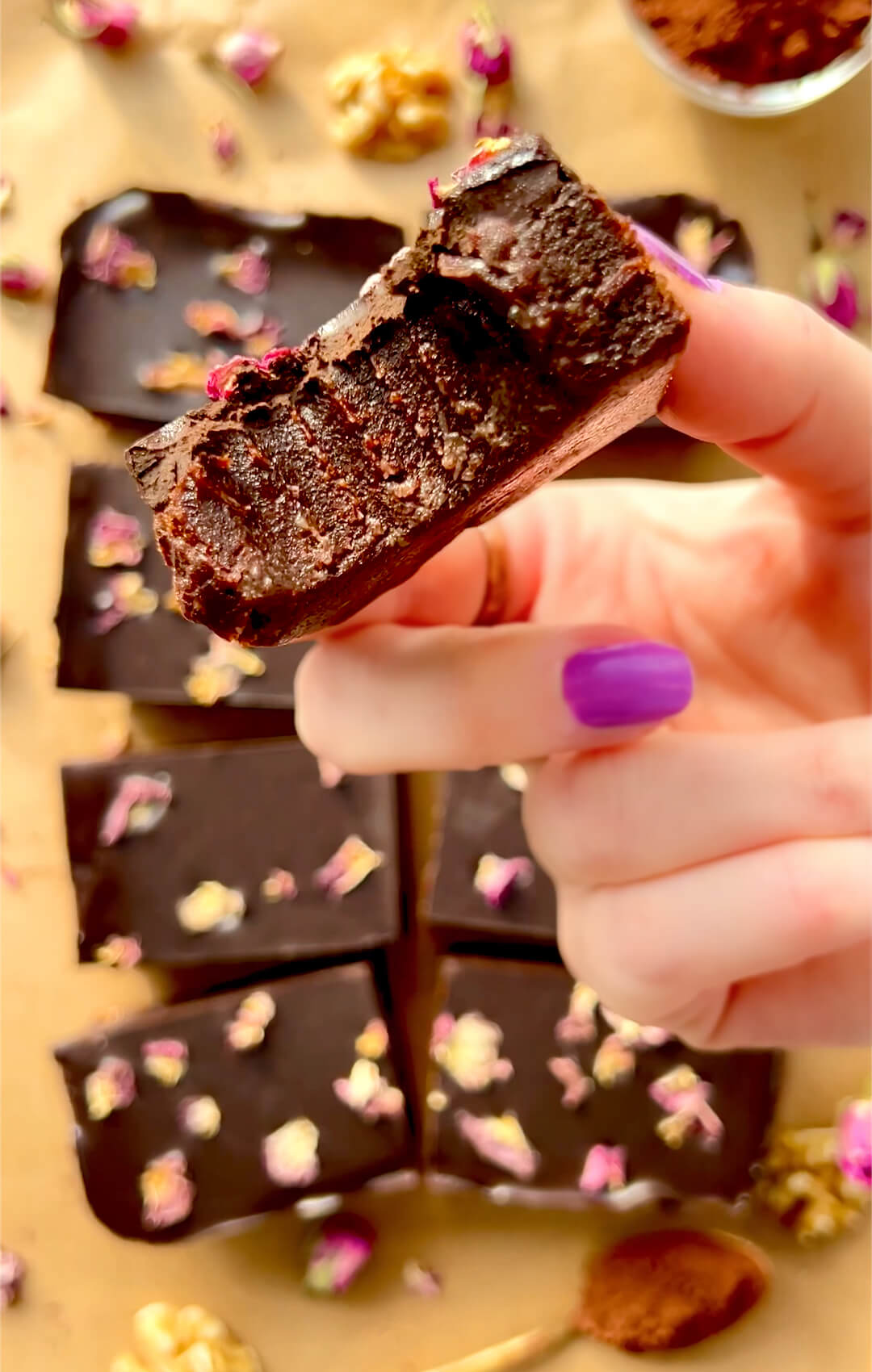 Close-up of a bitten healthy no-bake date brownie held in hand, showing tooth marks and a gooey fudgy chocolate center beneath the glossy ganache, rich and deeply chocolatey, naturally sweetened, paleo, gluten-free, and made with no refined sugar, perfect for a sweet snack or dessert. These are quick and easy to make and perfect for meal prep .