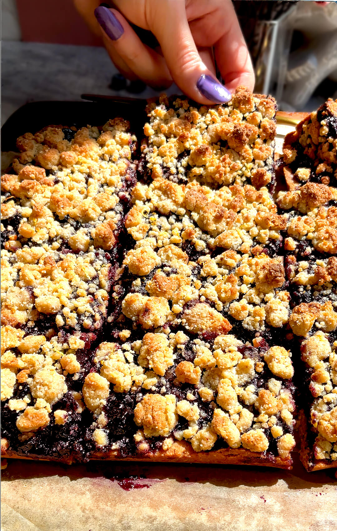 A slice of healthy blueberry crumble bars being lifted to show the thick jammy blueberry sauce filling and golden buttery crumble topping, gluten-free, dairy-free, paleo friendly and refined sugar-free.