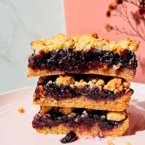 Stacked healthy blueberry crumble bars showing the rich jammy and shiny blueberry sauce layer with whole berries and a tender buttery base under a golden crumble topping, gluten-free, grain-free, dairy-free and paleo friendly with vegan option. made with almond flour, coconut flour, coconut sugar, coconut oil and lemon zest.