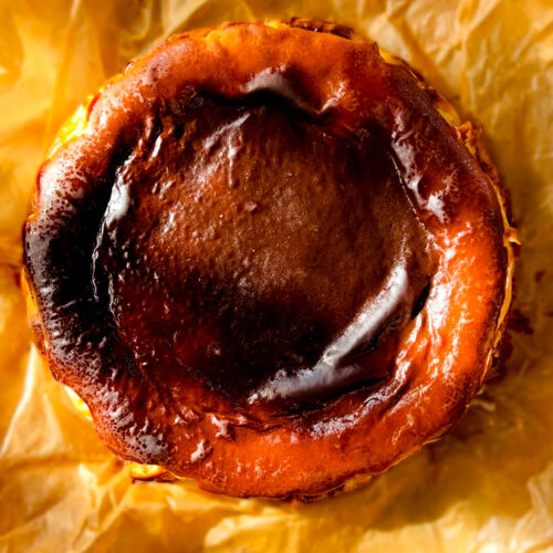 Overhead photo of a Basque Burnt Cheesecake with a dark caramelised top, golden rustic edges, and crinkled baking paper.