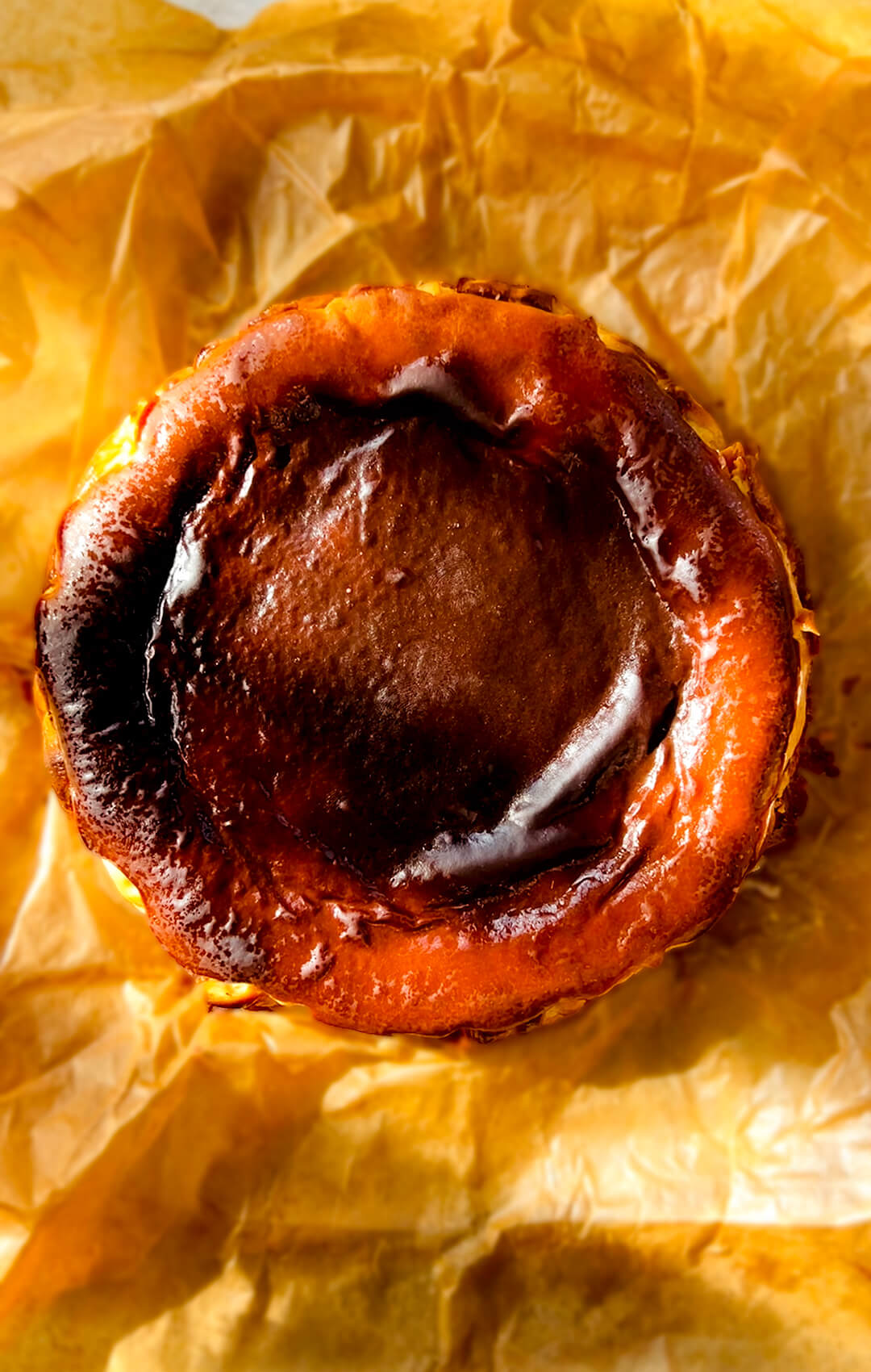 Overhead photo of a Basque Burnt Cheesecake with a dark caramelised top, golden rustic edges, and crinkled baking paper.