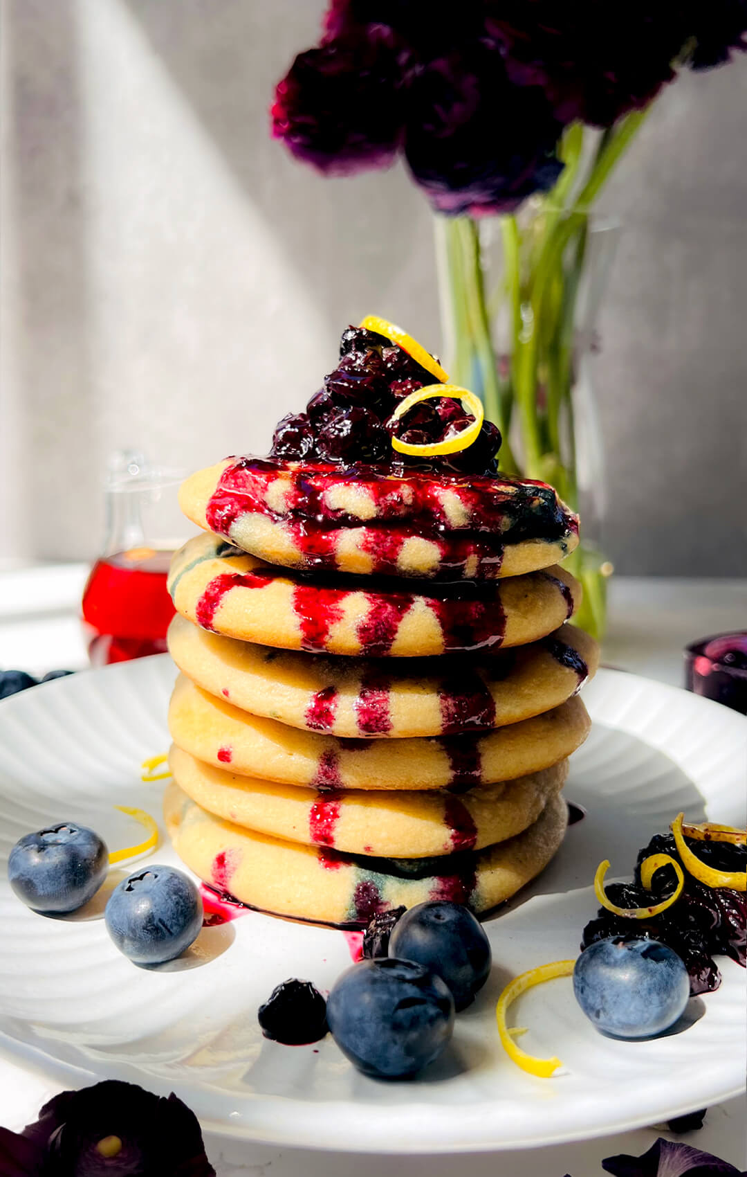 Tall stack of fluffy paleo blueberry pancakes topped with blueberry sauce and lemon zest, on a white plate, showing a soft, thick texture, juicy blueberries, and a healthy weekend breakfast or brunch recipe. These pancake are gluten-free, dairy-free, grain-free, refined sugar-free and vegetarian.