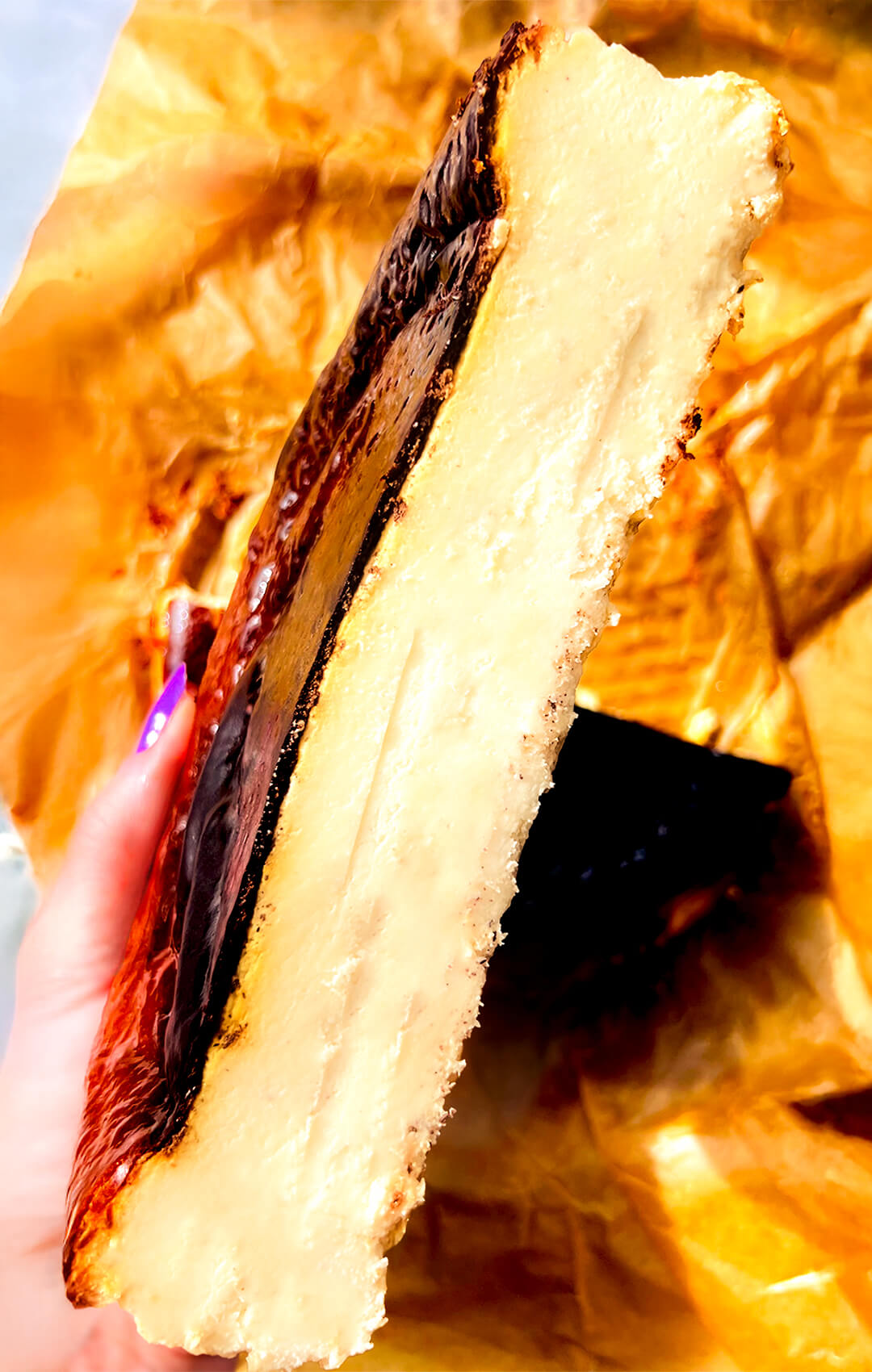 Close-Up of Basque Burnt Cheesecake slice to a half, its thick slice, showing a creamy, smooth centre with a dark caramelised top and golden edges.