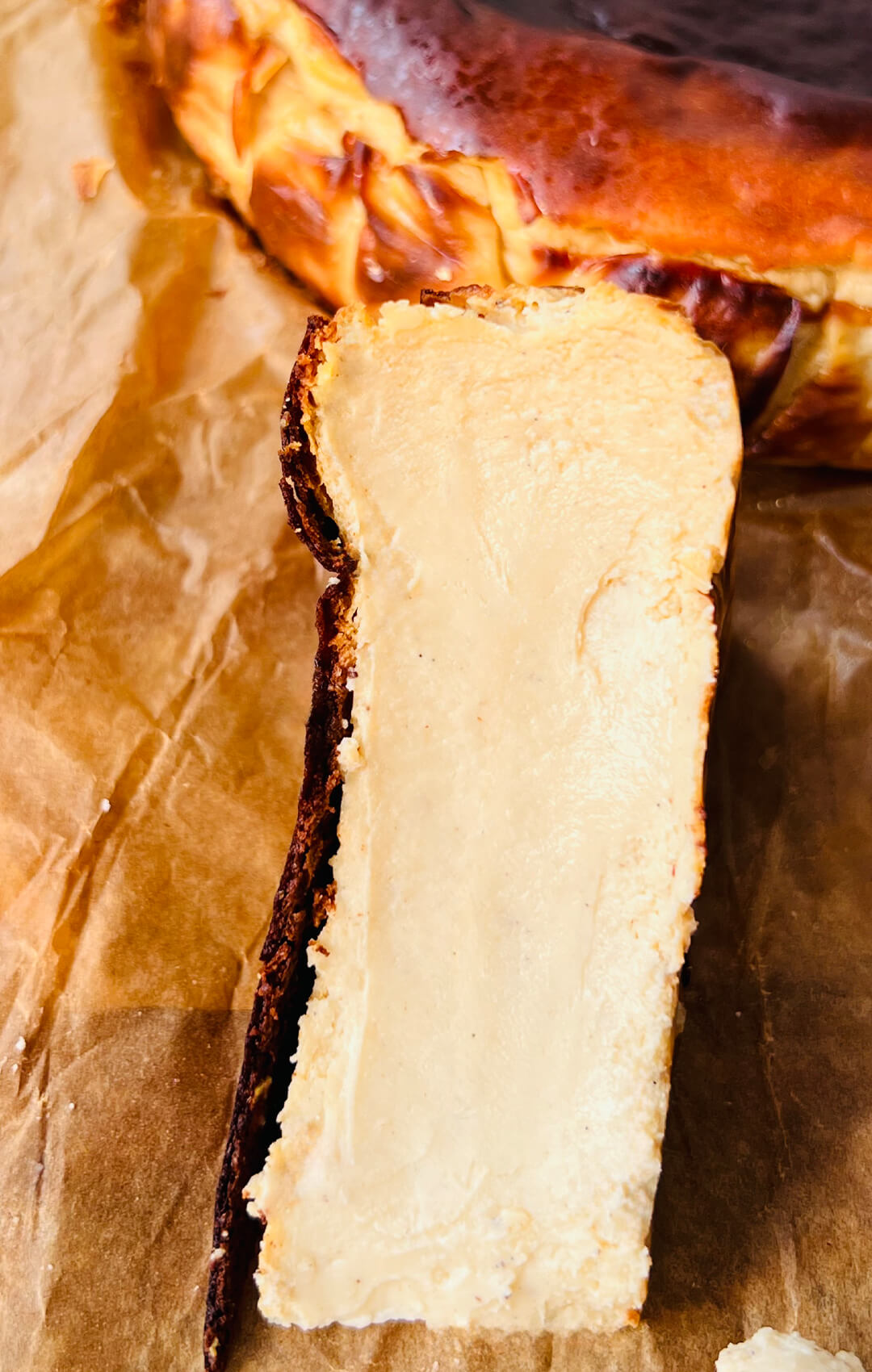 Close-Up to a Tall slice of refined sugar-free Basque Burnt Cheesecake with a creamy vanilla centre and dark caramelised crust.