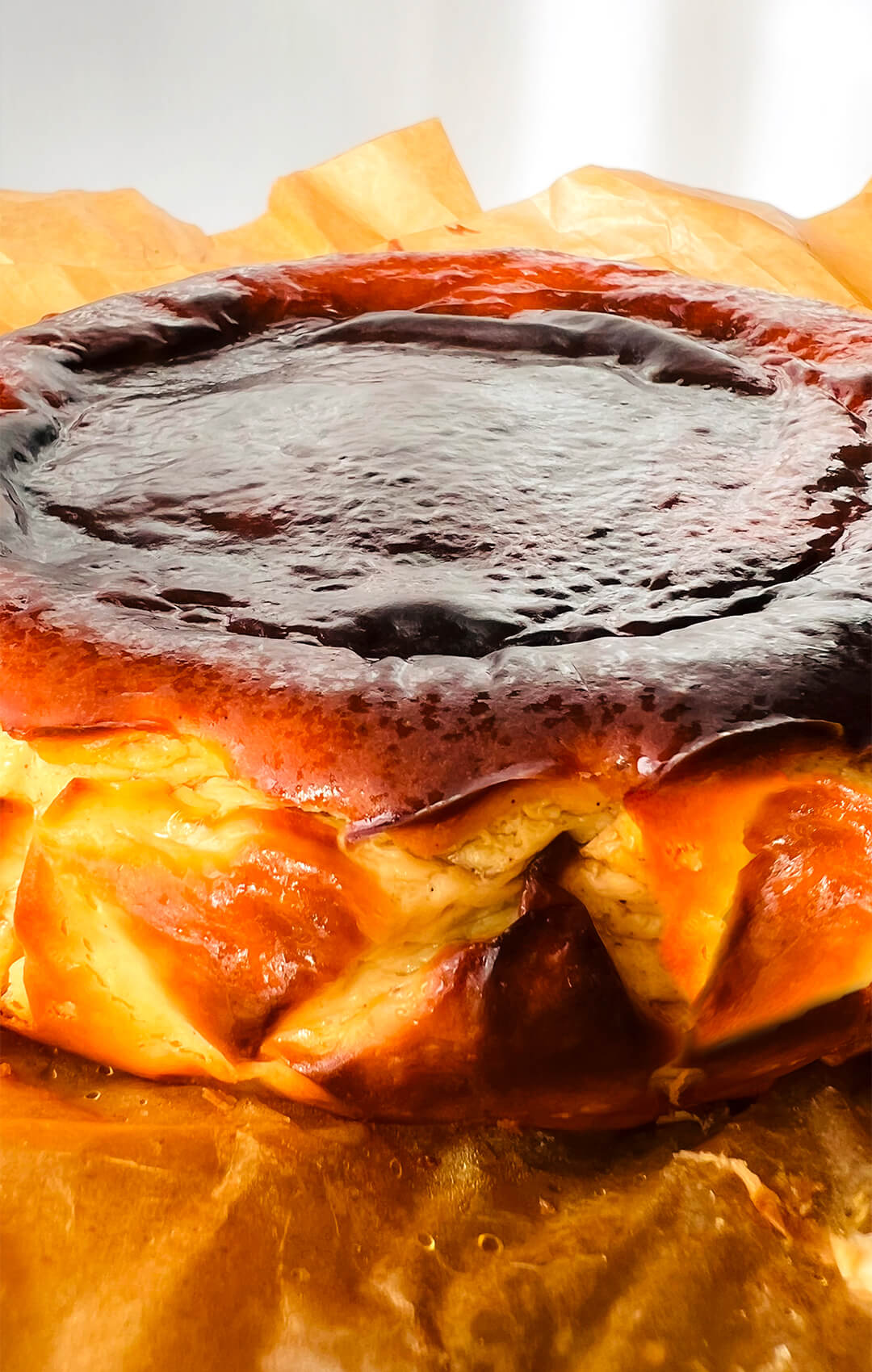 Side view of a Basque Burnt Cheesecake with a dark caramelised top, golden wrinkled sides, and rustic crinkled baking paper.