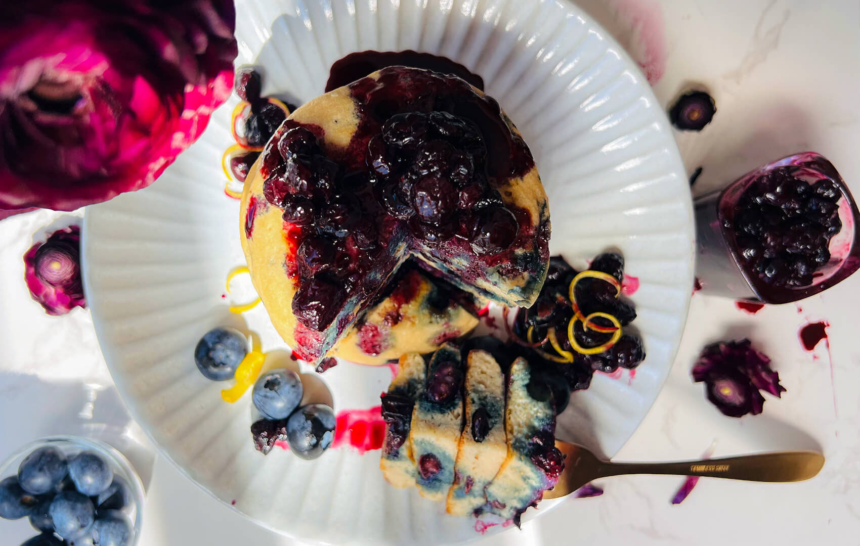 Overhead view of fluffy paleo blueberry pancakes with blueberry sauce on a white plate, showing a soft, thick, pillowy texture, juicy blueberries, and a cozy healthy weekend brunch presentation.