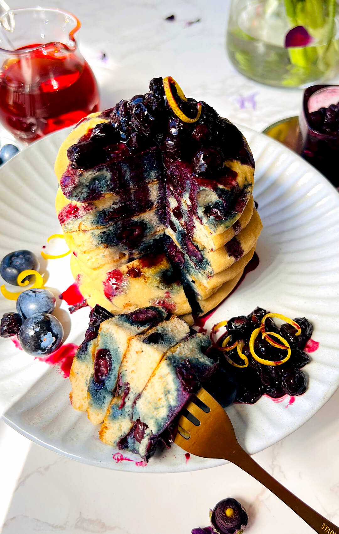 Plated fluffy paleo blueberry pancakes with blueberry sauce and a sliced piece in front, showing a soft, tender inside, juicy blueberries, thick texture, and a healthy gluten-free dairy-free grain-free breakfast.